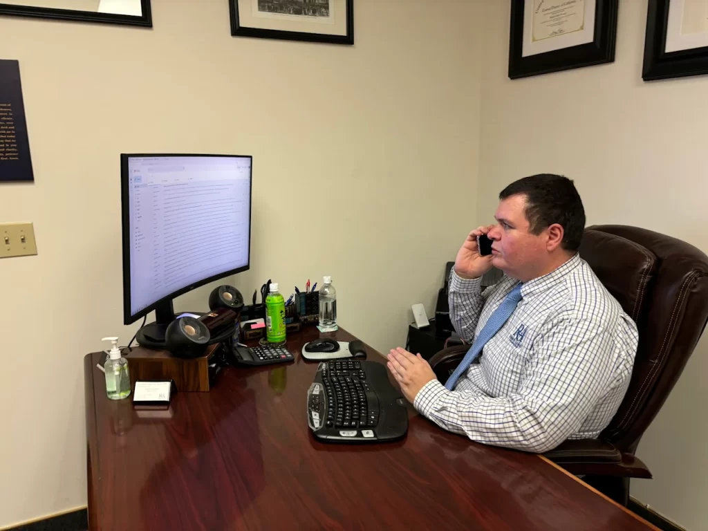 Immigration attorney speaking on the phone at his desk while reviewing emails on a computer screen.